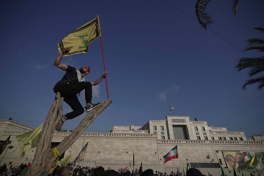 A Hezbollah supporter takes a selfie while waving a Hezbollah flag as he stands on a tree outside the Iranian Embassy in Beirut, Lebanon, Wednesday, June 25, 2025 (AP)