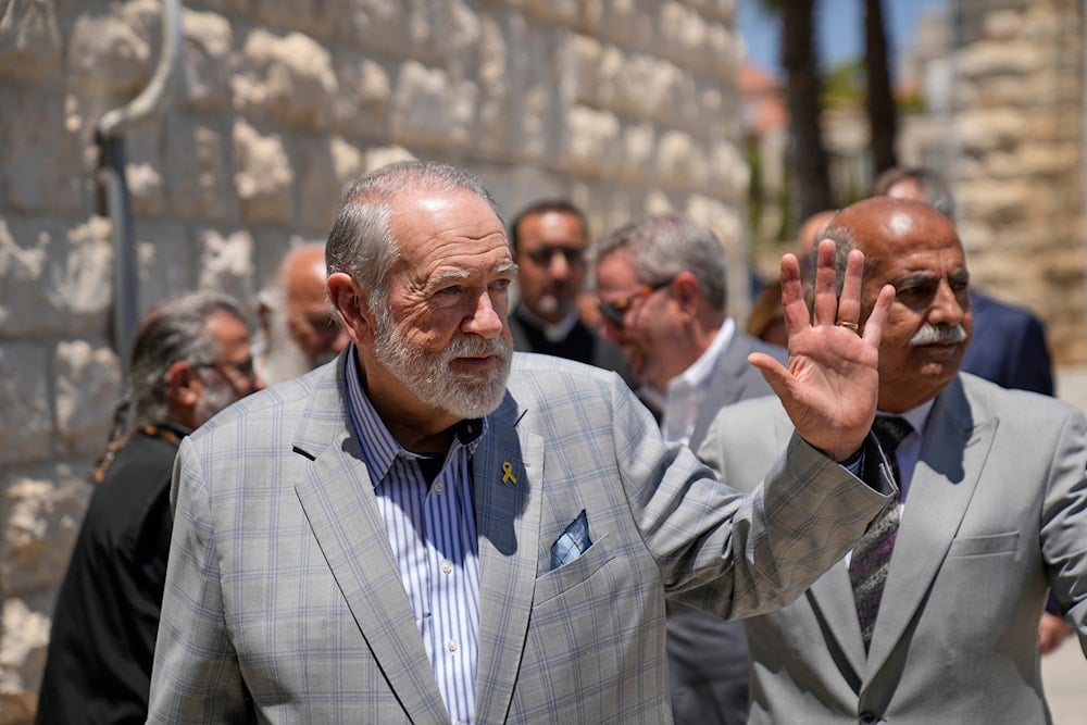 US Ambassador to 'Israel' Mike Huckabee waves upon his arrival in the West Bank town of Taybeh, east of Ramallah Saturday, July 19, 2025 (AP)