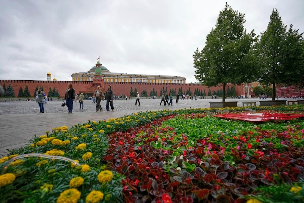 People walk past flowers during an annual flower festival outside the GUM department store in Red Square with the Kremlin in the background in Moscow, Russia, Tuesday, July 1, 2025. (AP)