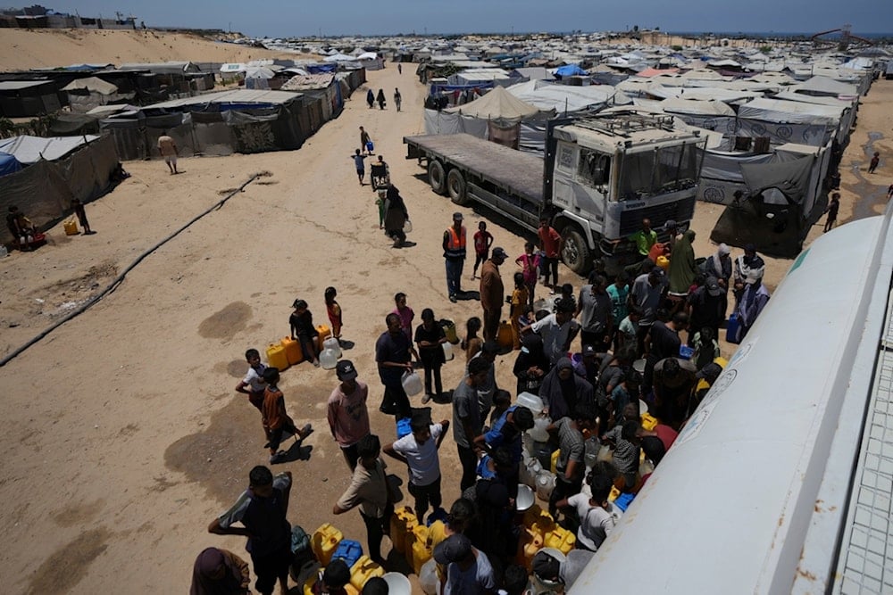 Displaced Palestinians gather to collect water from a truck at a makeshift tent camp in Khan Younis, southern Gaza Strip, Saturday, July 19, 2025 (AP)