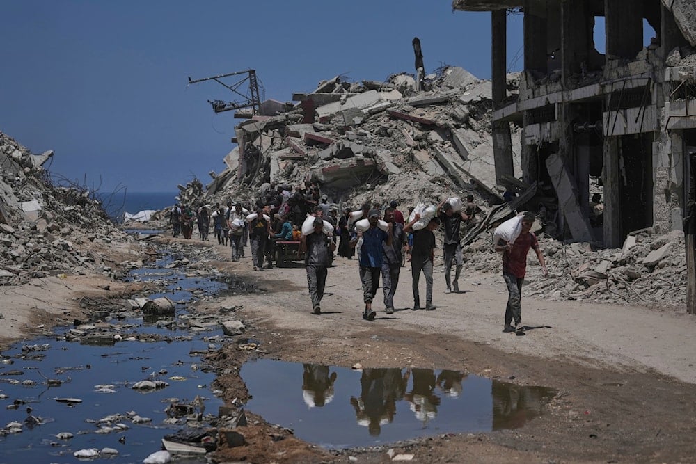 Palestinians carry sacks of flour unloaded from a humanitarian aid convoy that reached Gaza City from the northern Gaza Strip, Tuesday, July 22, 2025 (AP)