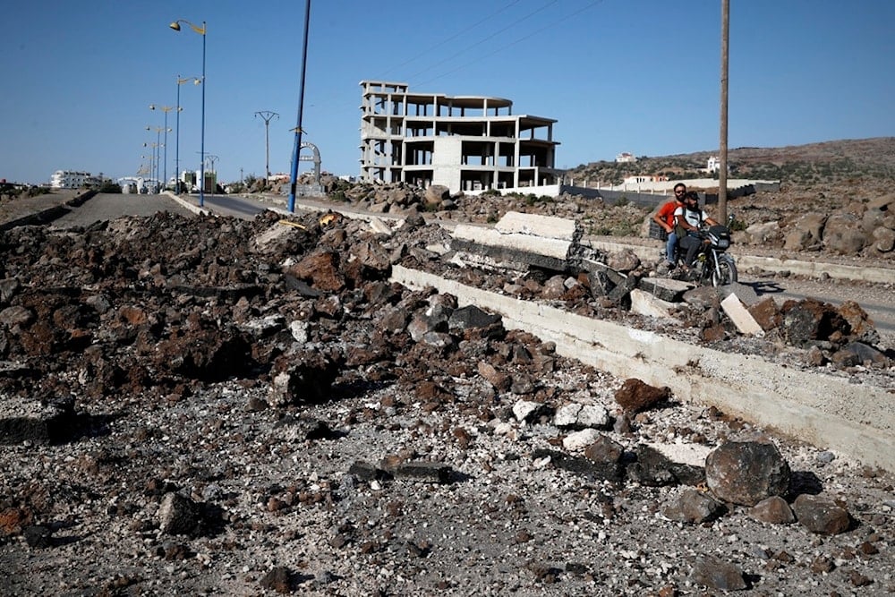 Druze militiamen ride a motorcycle past the site of an Israeli strike last week on the main road outside the town of Sweida, Syria, Friday, July 25, 2025 (AP)