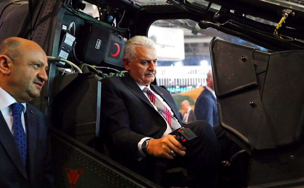 Turkey's Prime Minister Binali Yildirim, centre, sits at a helicopter gunship, during a visit at the IDEF’17, the International Defence Industry Fair in Istanbul, as Turkey's Defence Minister Fikri Isik, left, looks on, Tuesday, May 9, 2017 (AP)