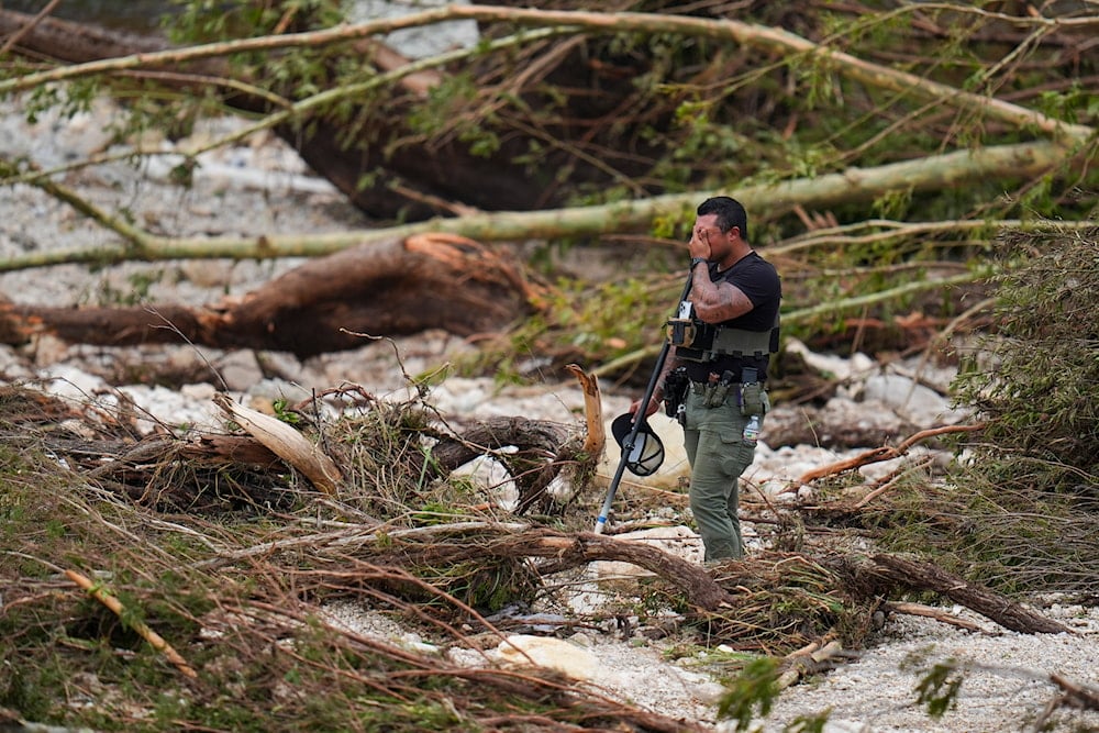 A Sheriff's deputy pauses while combing through the banks of the Guadalupe River near Camp Mystic after a flash flood swept through the area on July 5, 2025, in Hunt, Texas. (AP Photo/Julio Cortez)
