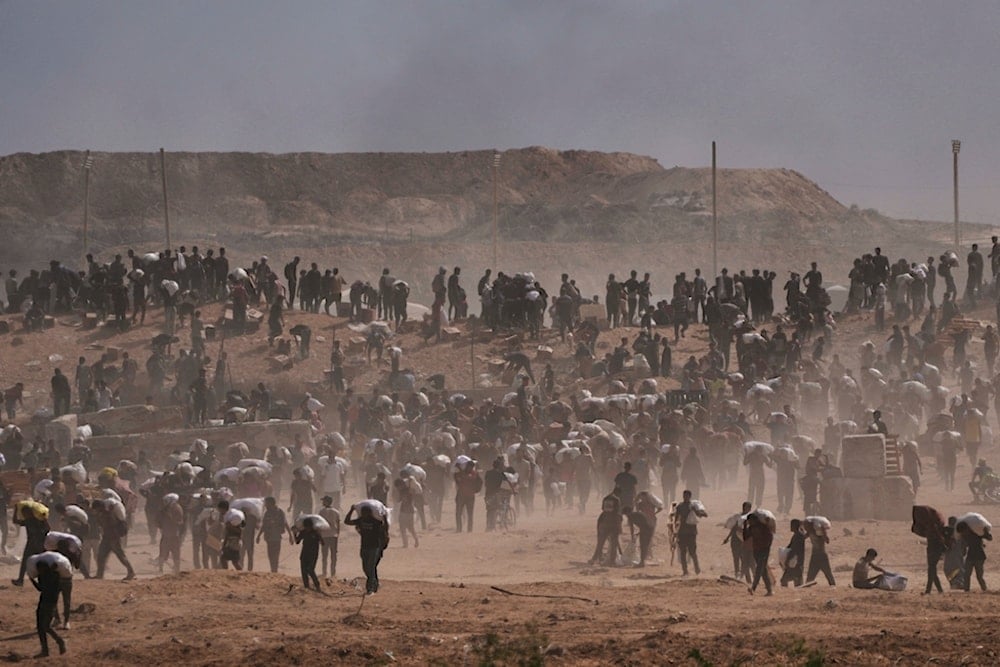 Palestinians carry humanitarian aid packages near a Gaza Humanitarian Foundation distribution center operated by the US-backed organization, in Netzarim, central Gaza Strip, Monday, August 4, 2025 (AP)