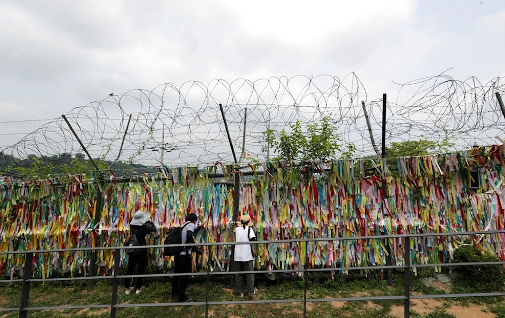 Visitors look through a wire fence decorated with ribbons written with messages wishing for the reunification of the two Koreas at the Imjingak Pavilion in Paju, South Korea, Sunday, June 30, 2019 (AP)