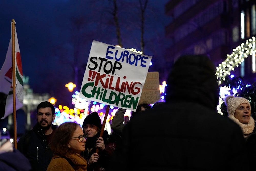 A protestor holds a sign during a demonstration calling for a ceasefire in Gaza outside of an EU summit in Brussels, Thursday, Dec. 14, 2023 (AP)
