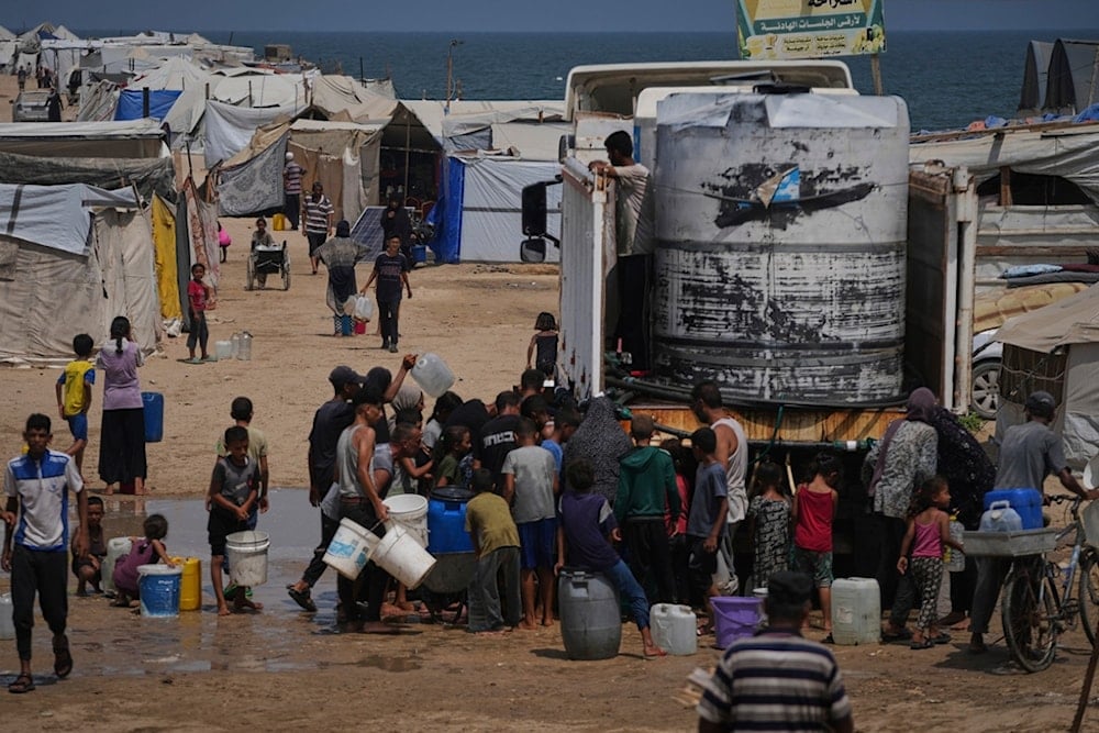 Displaced Palestinians gather to collect water from a truck during a heat wave at a makeshift tent camp in Khan Younis, Gaza Strip, Wednesday, August 13, 2025 (AP)