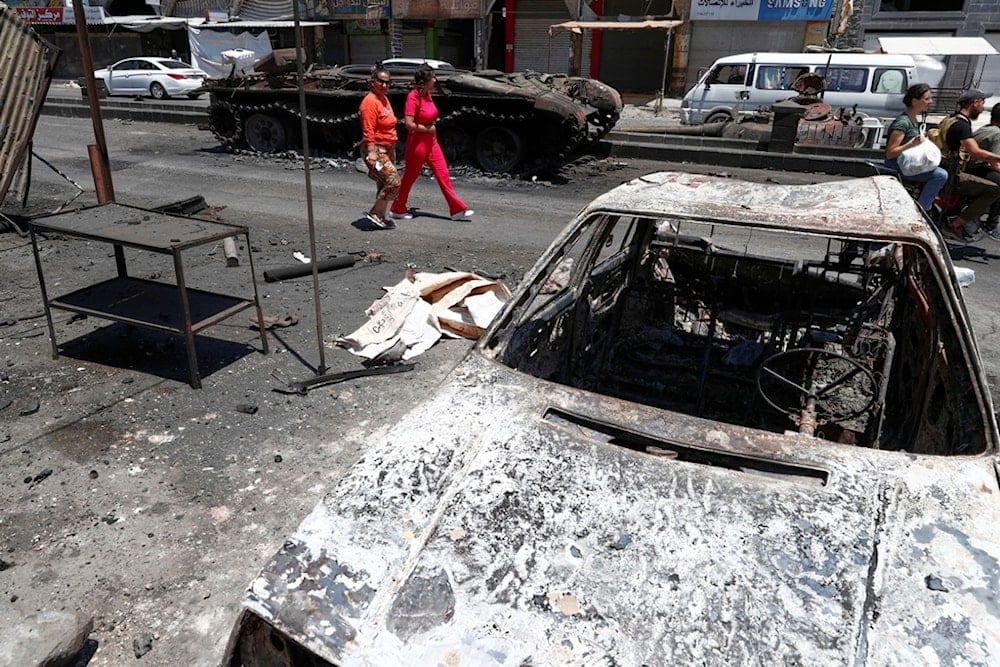 Residents walk by burned-out cars and a military vehicle following last week's sectarian clashes in the Druze-majority town of Sweida, Syria, Friday, July 25, 2025. (AP Photo/Omar Sanadiki)