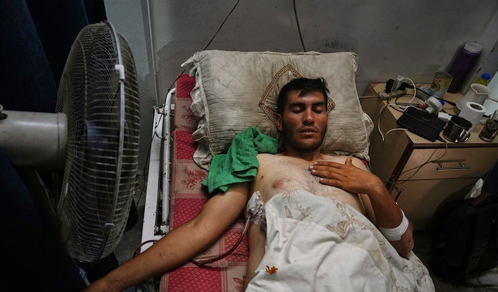 A Palestinian patient seeks relief from the heat by sitting near a fan during a heat wave, inside a warehouse set up in the yard of Shifa Hospital in Gaza City, Wednesday, Aug. 13, 2025. (AP)