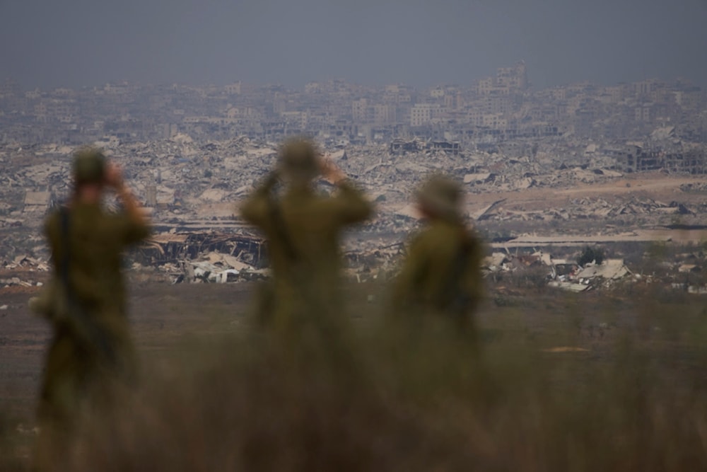 Israeli soldiers use binoculars to look at damaged buildings in the Gaza Strip, from southern occupied Palestine, Wednesday, August 13, 2025 (AP)
