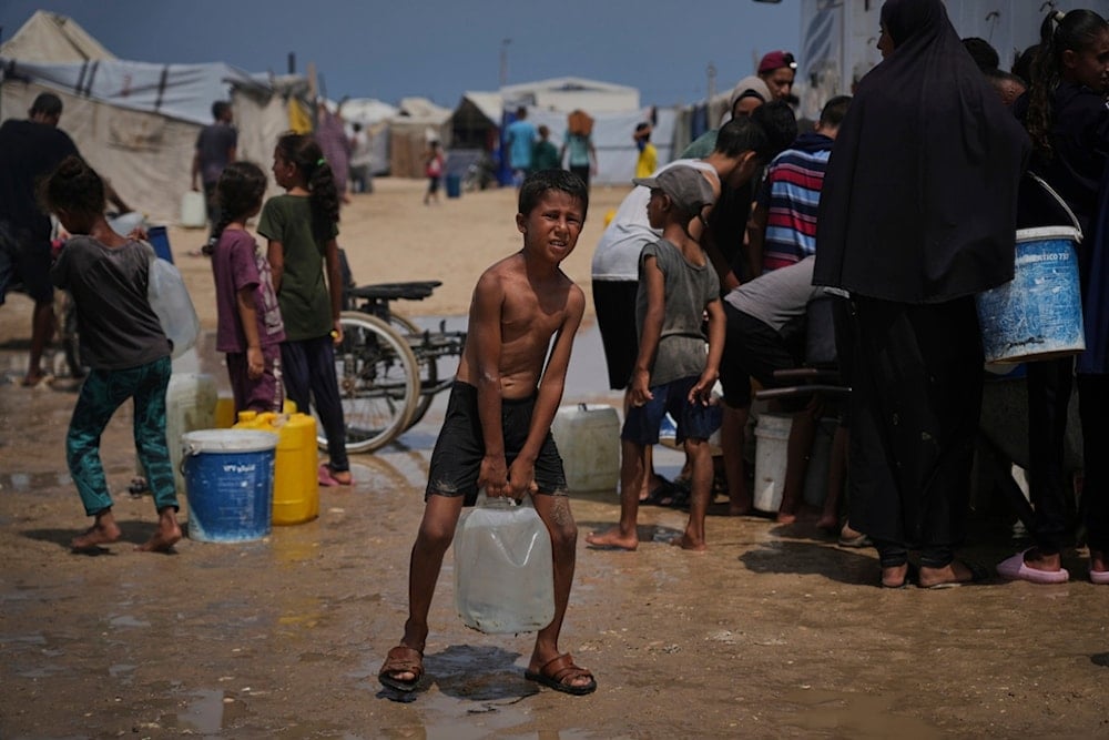Displaced Palestinians gather to collect water from a truck during a heat wave at a makeshift tent camp in Khan Younis, Gaza Strip, Wednesday, August 13, 2025 (AP)