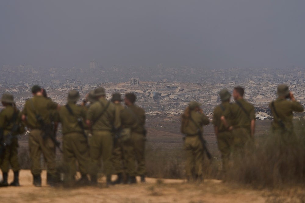 Israeli soldiers uses binoculars to look at damaged buildings in the Gaza Strip, from southern Israel, Wednesday, Aug. 13, 2025 (AP)