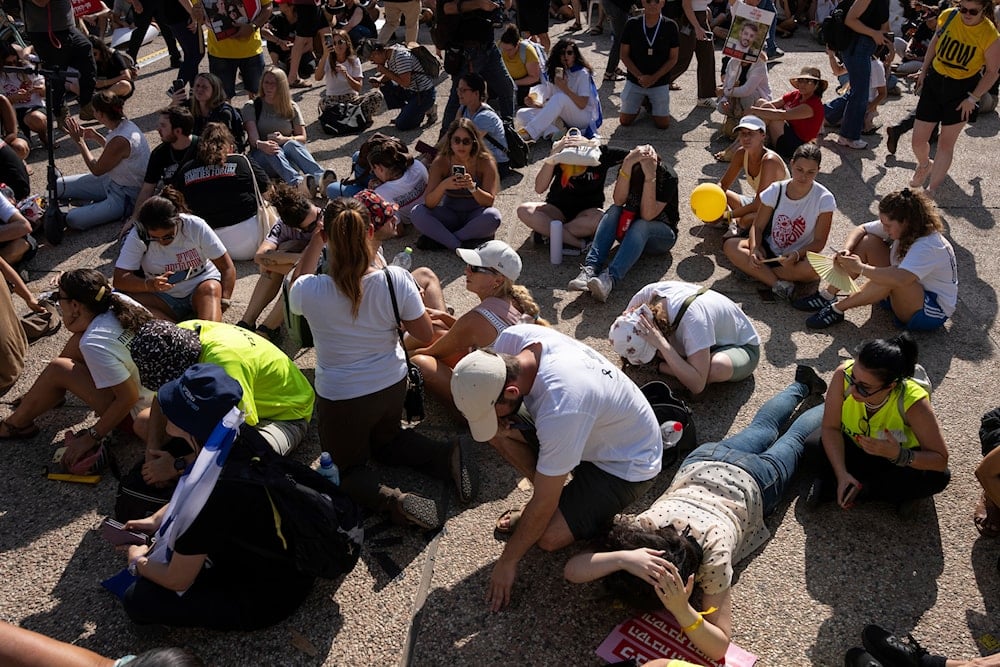 People sit on the ground and cover their heads as a siren sounds a warning of incoming missile fired from Yemen in Tel Aviv, Occupied Palestine, Sunday, Aug. 17, 2025 (AP)