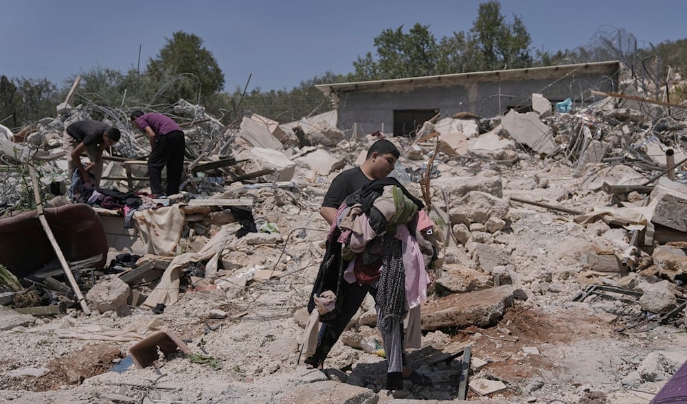 A Palestinian youth carries clothes as he walks over the rubble of a house demolished by the Israeli army in the West Bank village of Beit Sira, near Ramallah, Tuesday, Aug. 19, 2025. (AP)