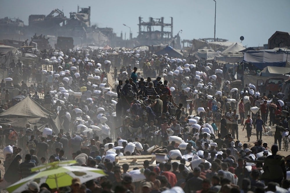 Palestinians carry sacks of flour taken from a humanitarian aid convoy en route to Gaza City, in the outskirts of Beit Lahiya, northern Gaza Strip, Friday, August 1, 2025 (AP)