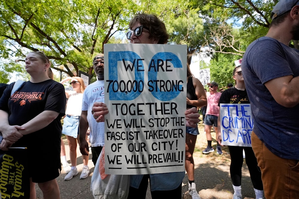 Activists carry signs during a protest against President Donald Trump's federal takeover of policing of the District of Columbia, Saturday, Aug. 16, 2025, in Washington. (AP Photo/Alex Brandon)