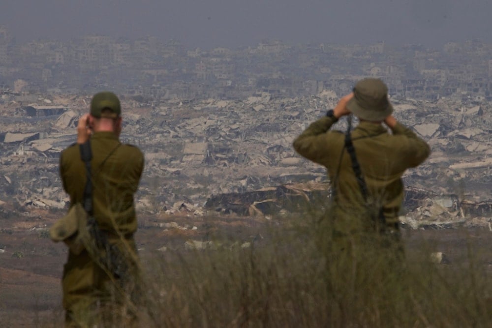 Israeli soldiers uses binoculars to look at damaged buildings in the Gaza Strip, from southern occupied Palestine, Wednesday, Aug. 13, 2025. (AP Photo/Ariel Schalit)