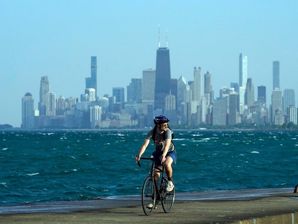 A person rides a bike on a breakwater along Lake Michigan against downtown skyline Tuesday, May 21, 2024, in Chicago. (AP Photo/Kiichiro Sato)
