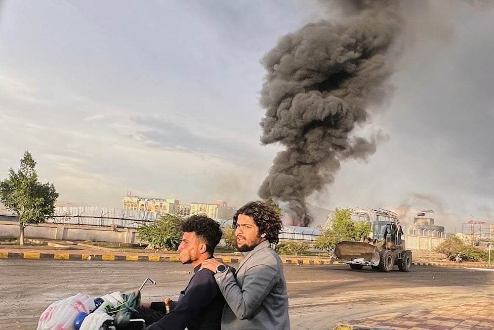 People ride a motorbike as smoke billows following Israeli airstrikes on multiple areas including a power planet and a gas station in Sanaa, Yemen, Sunday, Aug. 24, 2025 (AP)