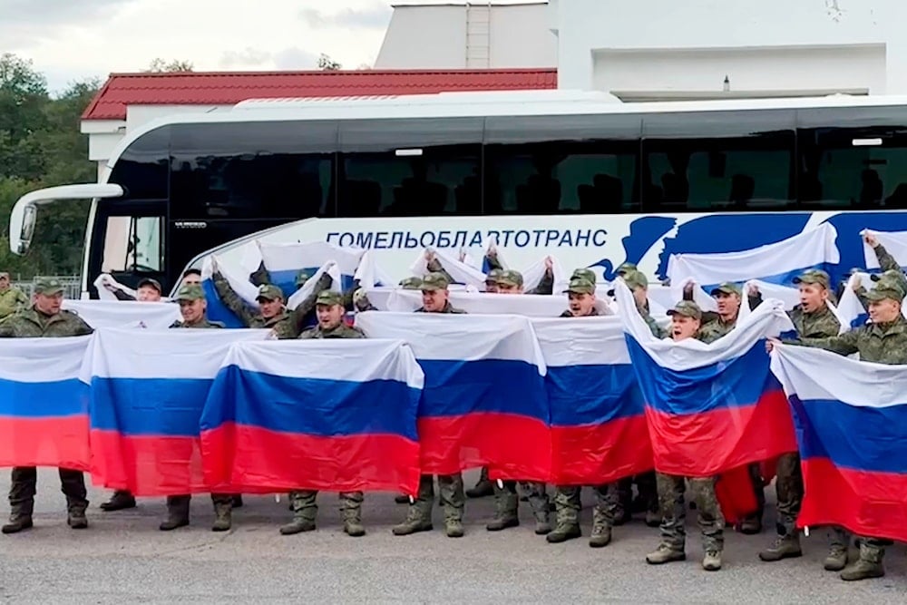 Freed Russian servicemen wave flags by a bus in Belarus after a prisoner exchange with Ukraine, August 24, 2025 (AP)