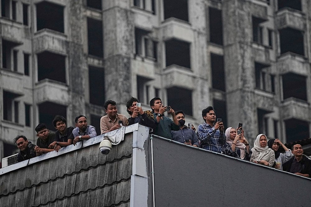 People watch a clash between protesters and riot police from the room of a building, during a protest against lavish allowances given to parliament members, in Jakarta, Indonesia, Monday, August 25, 2025. (AP Photo/Achmad Ibrahim)