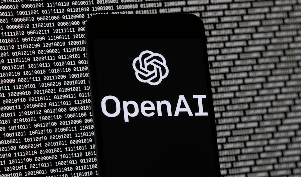 The OpenAI logo appears on a mobile phone in front of a computer screen with random binary data, March 9, 2023, in Boston. (AP)