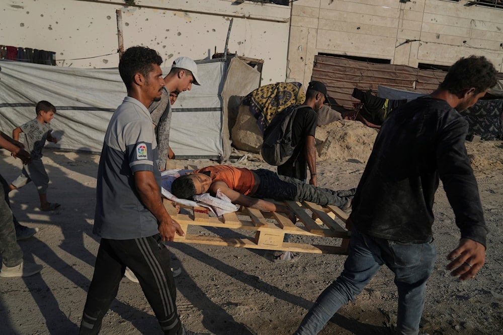 Palestinians carry the body of a boy who was killed while trying to reach a humanitarian aid convoy on the outskirts of Beit Lahiya, as they walk on a road in Gaza City, in the Gaza Strip, on August 24, 2025. (AP Photo/Abdel Kareem Hana)