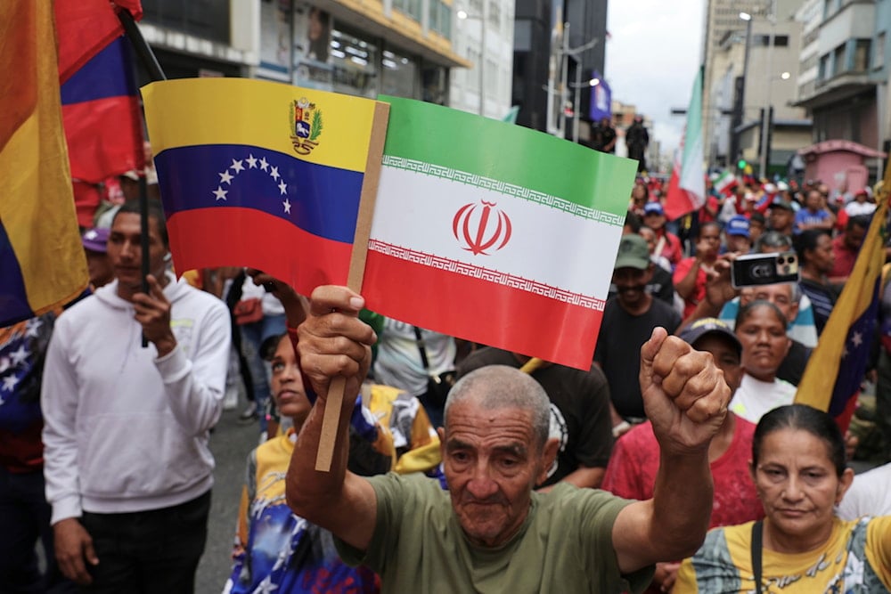 A man holds up a national flags from Venezuela and Iran, during a march against Israeli attacks on Iran, in Caracas, Venezuela, Thursday, June 19, 2025 (AP)