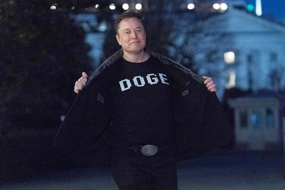 Elon Musk flashes his t-shirt that reads DOGE to the media as he walks on the South Lawn of the White House, in Washington, Sunday, March 9, 2025 (AP) 