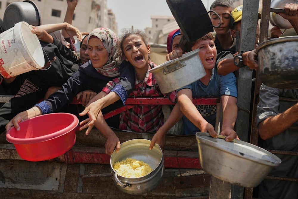 Palestinians struggle to get donated food at a community kitchen in Gaza City, northern Gaza Strip, Saturday, Aug. 16, 2025. (AP Photo/Jehad Alshrafi)