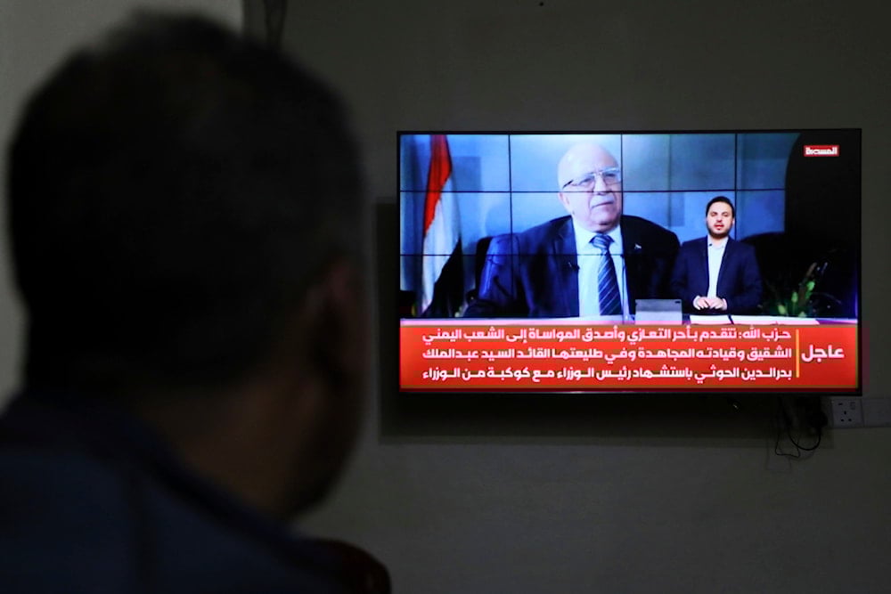 A man watches the news on TV, displaying footage of Ahmed al-Rahawi, the prime minister of the Sanaa government, who was killed, along with others, in Thursday's Israeli strikes on the capital, in Sanaa, Yemen, Saturday, August 30, 2025 (AP)
