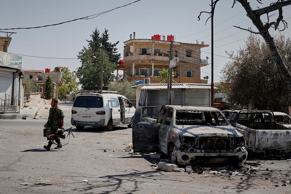 A Druze fighter carrying a machine gun walks past a burned-out car following last week's sectarian clashes in the Druze-majority town of Sweida, Syria, Friday, July 25, 2025 (AP)