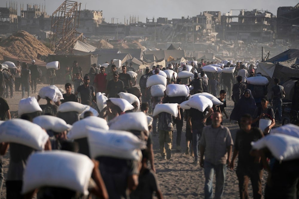 Palestinians carry sacks of flour unloaded from a humanitarian aid convoy en route to Gaza City from the northern Gaza Strip, Thursday, July 31, 2025 (AP)