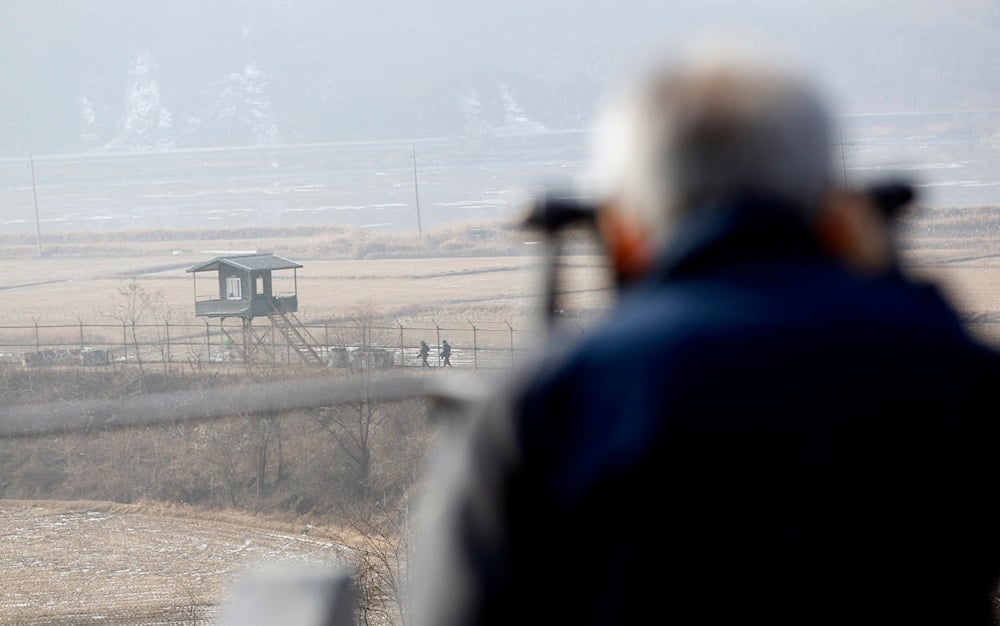 A visitor uses binoculars to watch north side as South Korean soldiers patrol near the border village of the Panmunjom (DMZ) that separates the two Koreas since the Korean War, in Paju, north of Seoul, South Korea, on December 29, 2011.