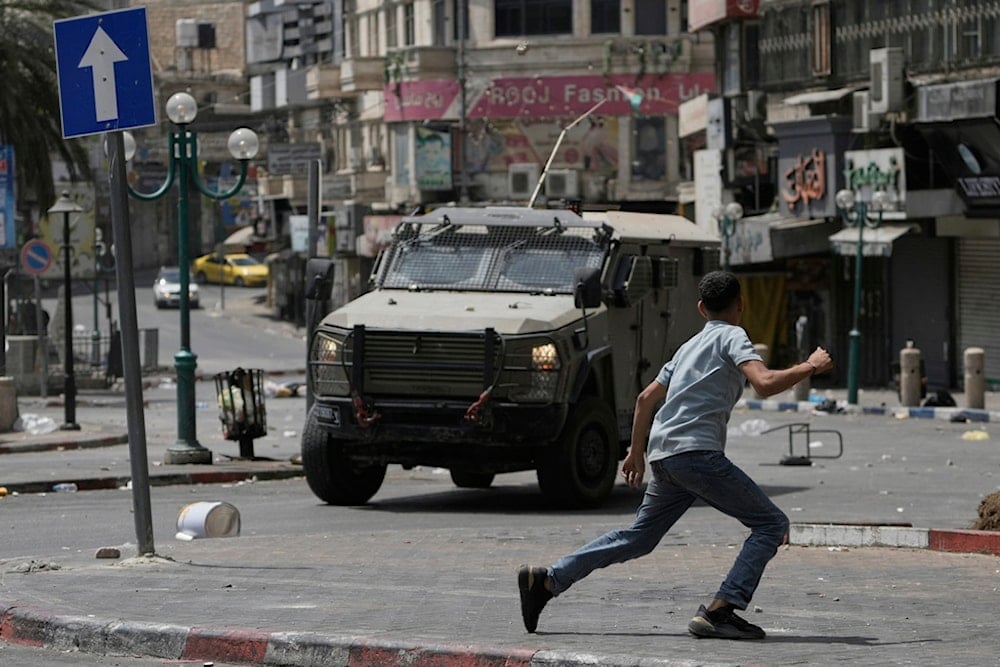 A Palestinian runs in front of an armored vehicle during clashes with Israeli forces following a military raid in the West Bank city of Nablus, Wednesday, August 27, 2025 (AP)
