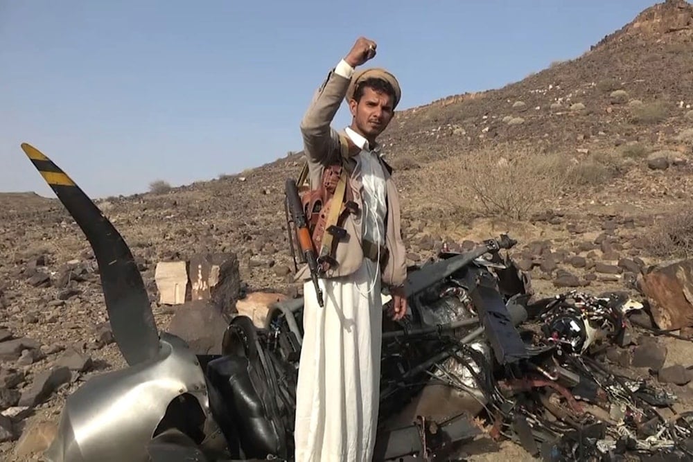 A Yemeni fighter celebrates in front of the debris of an American MQ9 aerial vehicle, shot down by the air defense forces of the Yemeni Armed Forces in Saada, Yemen, Friday, April, 26, 2024 (AP)