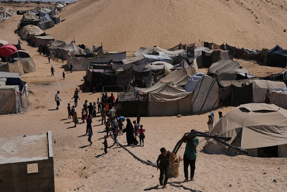 Displaced Palestinians walks through a tent camp in Muwasi, an area that Israel has designated as a safe zone, in Khan Younis southern Gaza Strip, Sunday, Sept. 21, 2025. (AP Photo/Jehad Alshrafi)