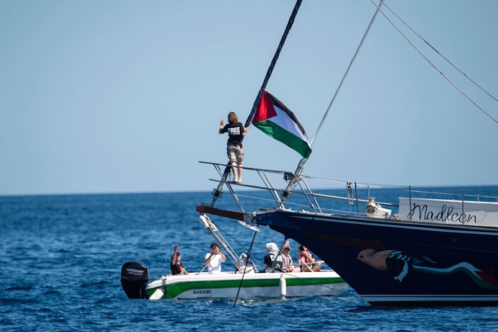 Climate activist Greta Thunberg stands near a Palestinian flag after boarding the Madleen boat and before setting sail for Gaza along with activists of the Freedom Flotilla Coalition, at the port of Catania, Italy, Sunday, June 1, 2025 (AP)