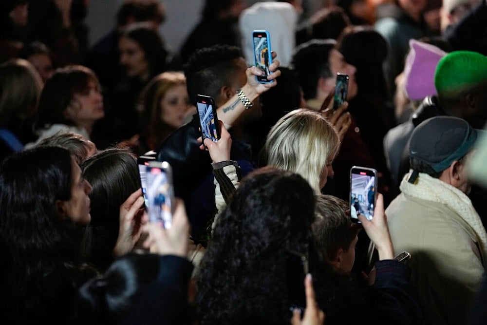 Spectators film with their phones models wearing creations as part of the ALUX9SM menswear Fall-Winter 2023-24 collection presented in Milan, Italy, Friday, January. 13, 2023. (AP Photo/Luca Bruno)