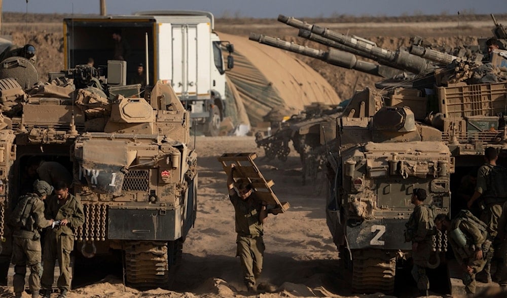 Israeli soldiers work on their armored vehicles parked in a staging area near the Gaza border, as seen from southern Palestine, Tuesday, Aug. 26, 2025. (AP)