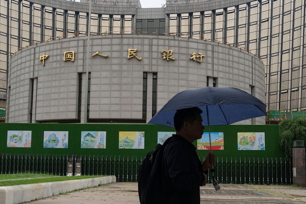 A man with an umbrella passes by China's central bank, or the People's Bank of China, in Beijing, Thursday, July 25, 2024. (AP Photo/Ng Han Guan)