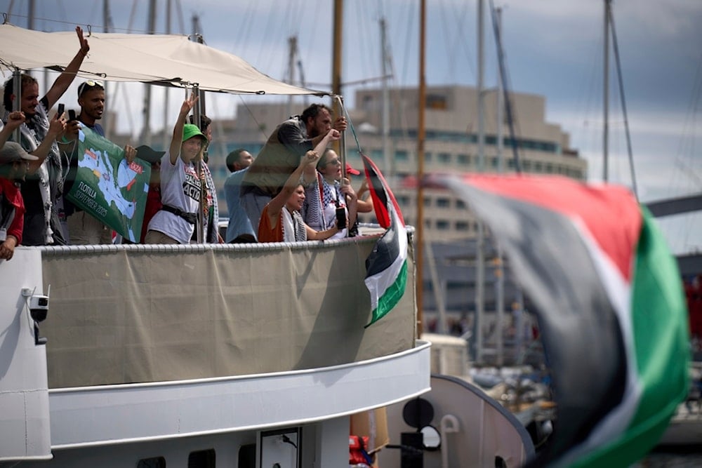 Swedish climate activist Greta Thunberg waves from a boat taking part in a civilian flotilla bound for Gaza, aiming to break the Israeli blockade and deliver humanitarian aid, in Barcelona, Spain, Sunday, August 31, 2025 (AP)