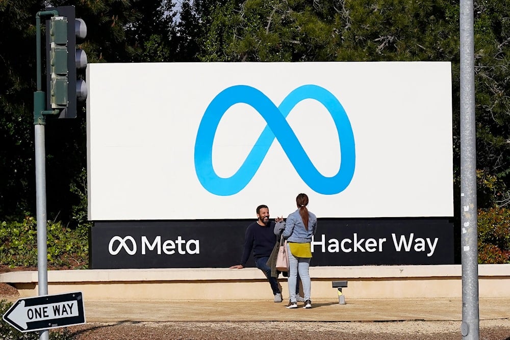 People talk near a Meta sign outside of the company's headquarters in Menlo Park, Calif., March 7, 2023 (AP)